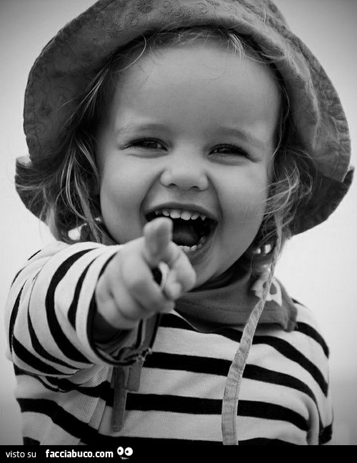 Bambina con cappello che indica e ride