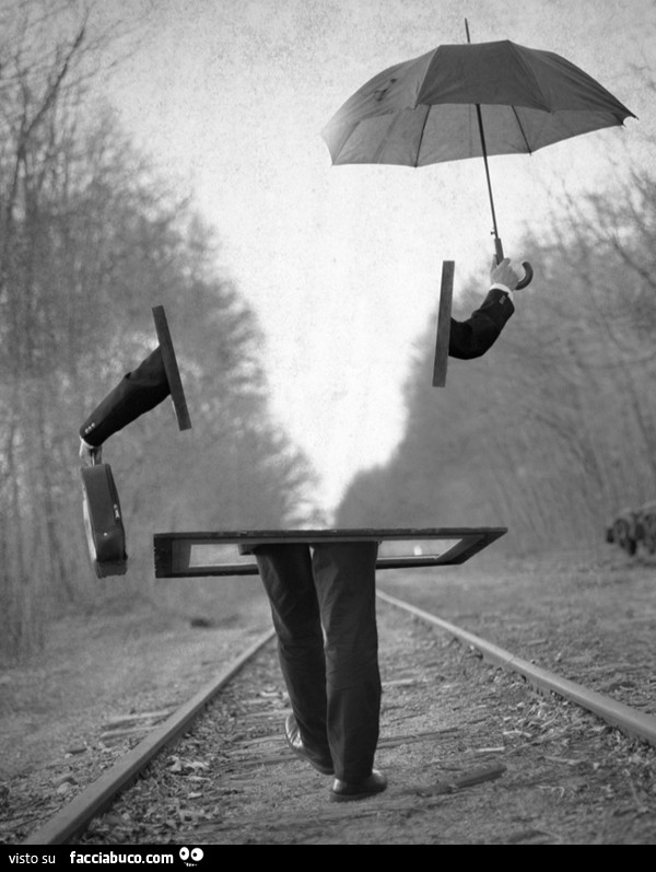 L'uomo che sparisce con l'ombrello e la valigetta in mano mentre cammina sui binari